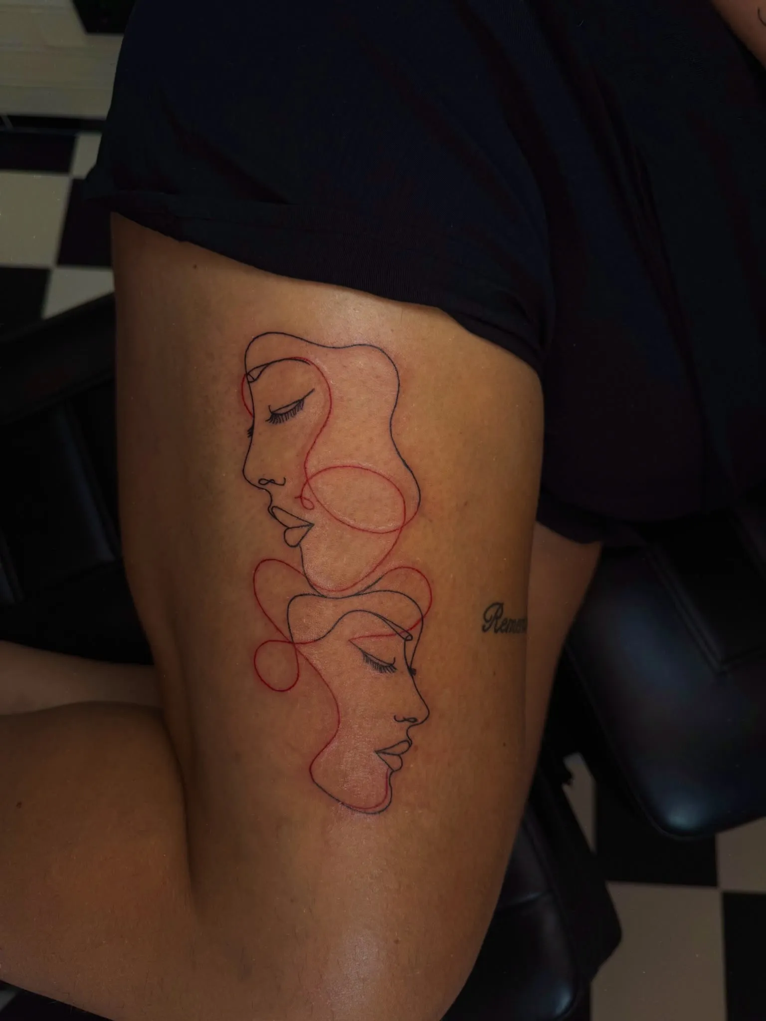 Fineline line-art tattoo van twee gezichten in zwarte en rode lijn op het bovenbeen