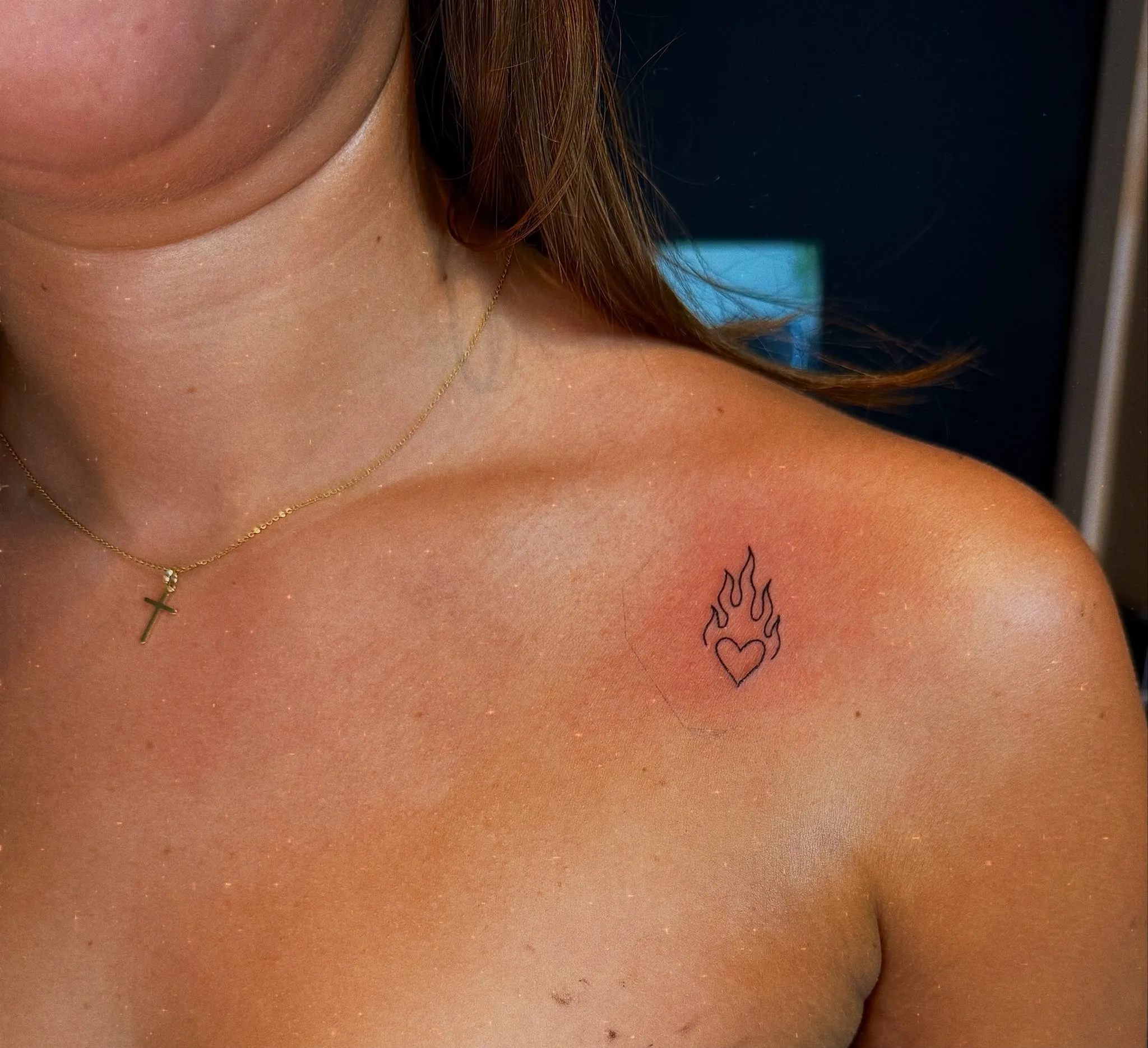 Kleine fineline tattoo van een hart met vlammen bij het sleutelbeen