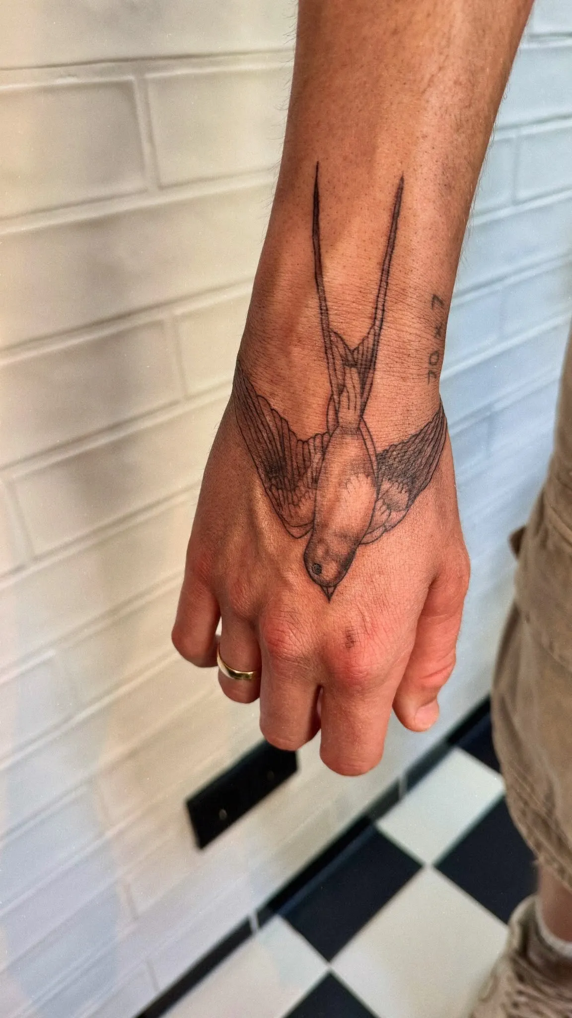 Fineline tattoo van een zwaluw met gespreide vleugels op de hand en pols