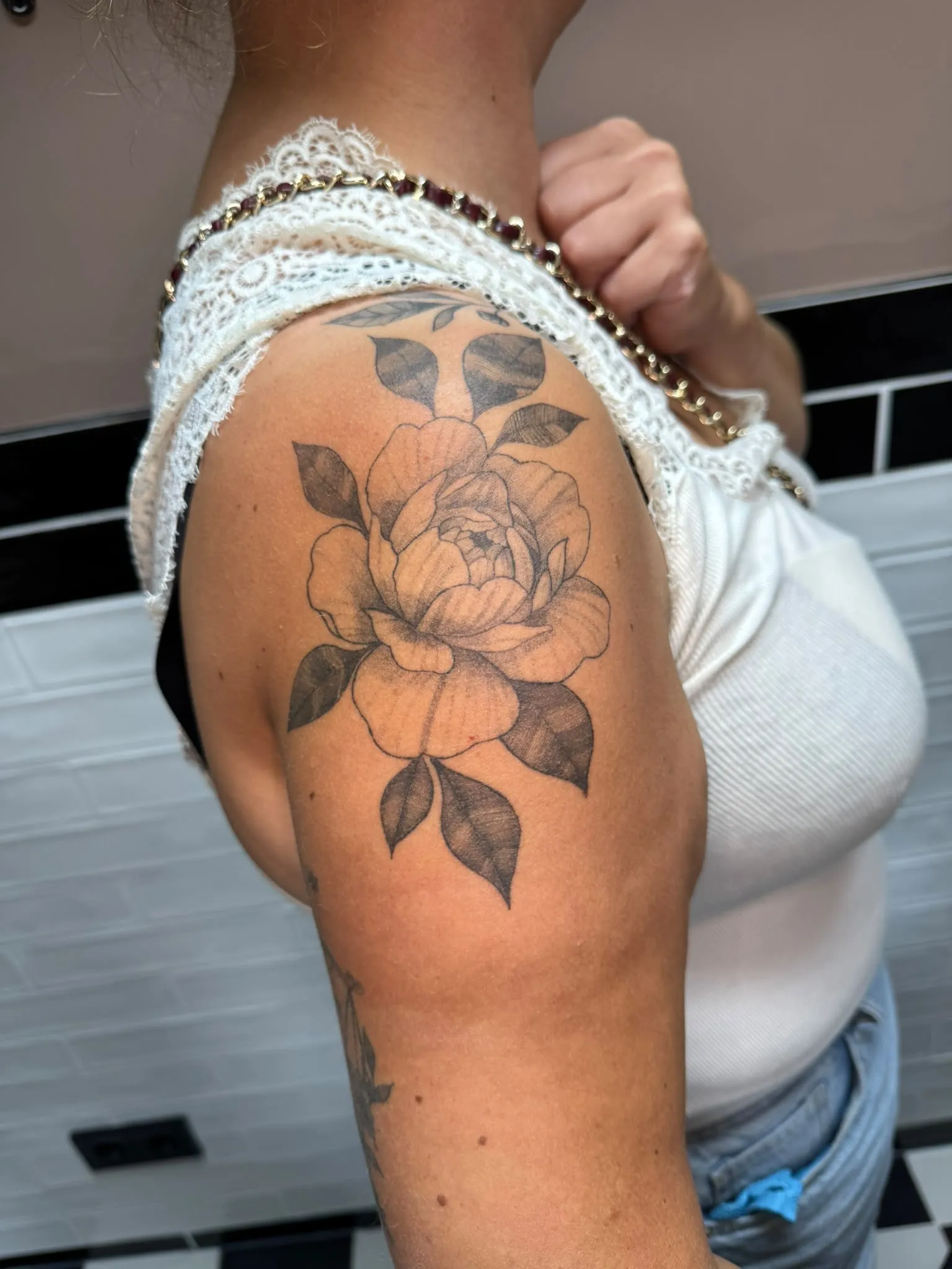 Floral tattoo van een pioenroos met gearceerde bladeren op de bovenarm, zwart-grijs