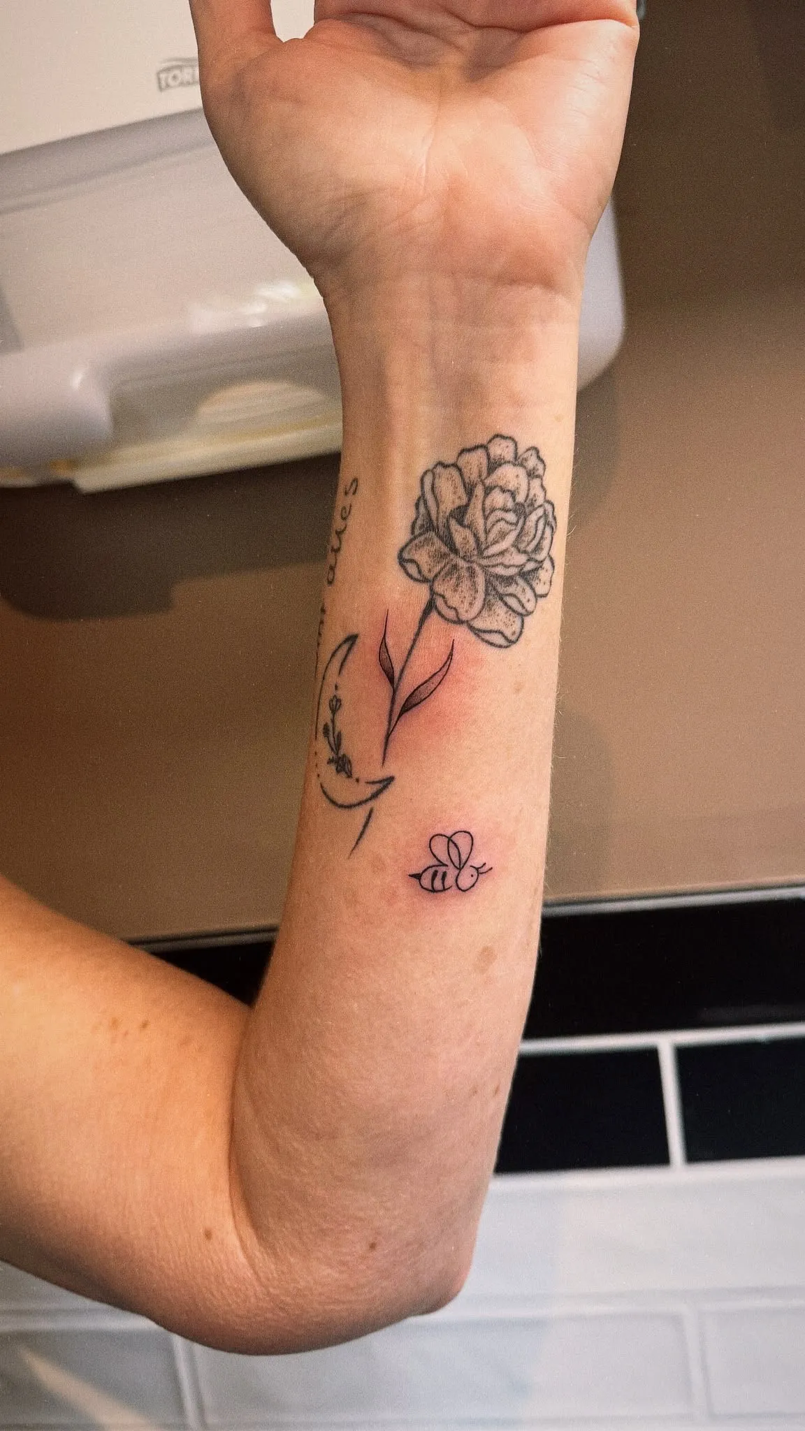 Floral tattoo van een pioen met een klein bijtje op de onderarm