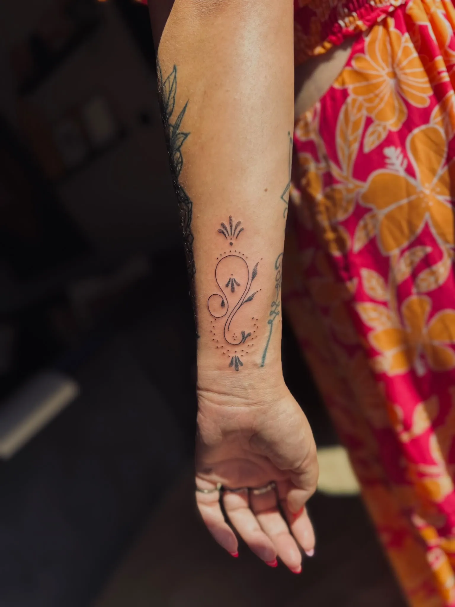 Ornamentale fineline tattoo met krul, blaadjes en stippellijnen op de onderarm, sieraad-achtig ontwerp