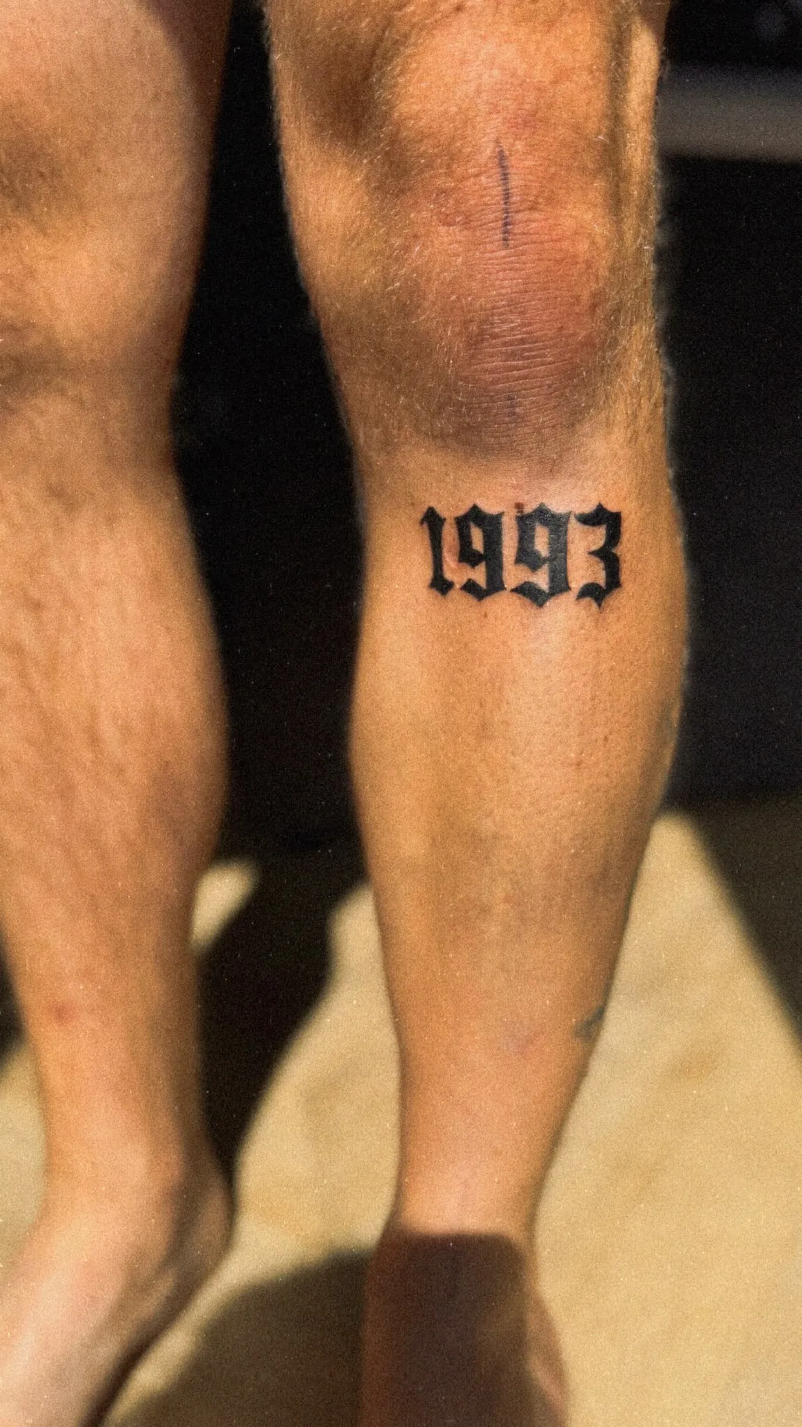 Tekst tattoo met het jaartal 1993 in gotische letters op het onderbeen