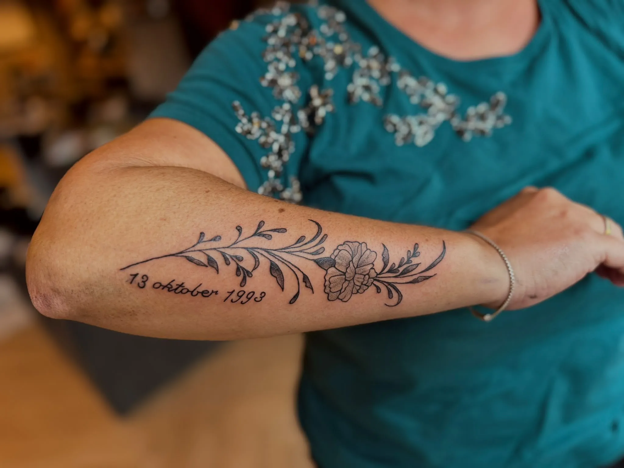 Tekst tattoo met de datum 13 oktober 1993 en een bloemenrank op de onderarm