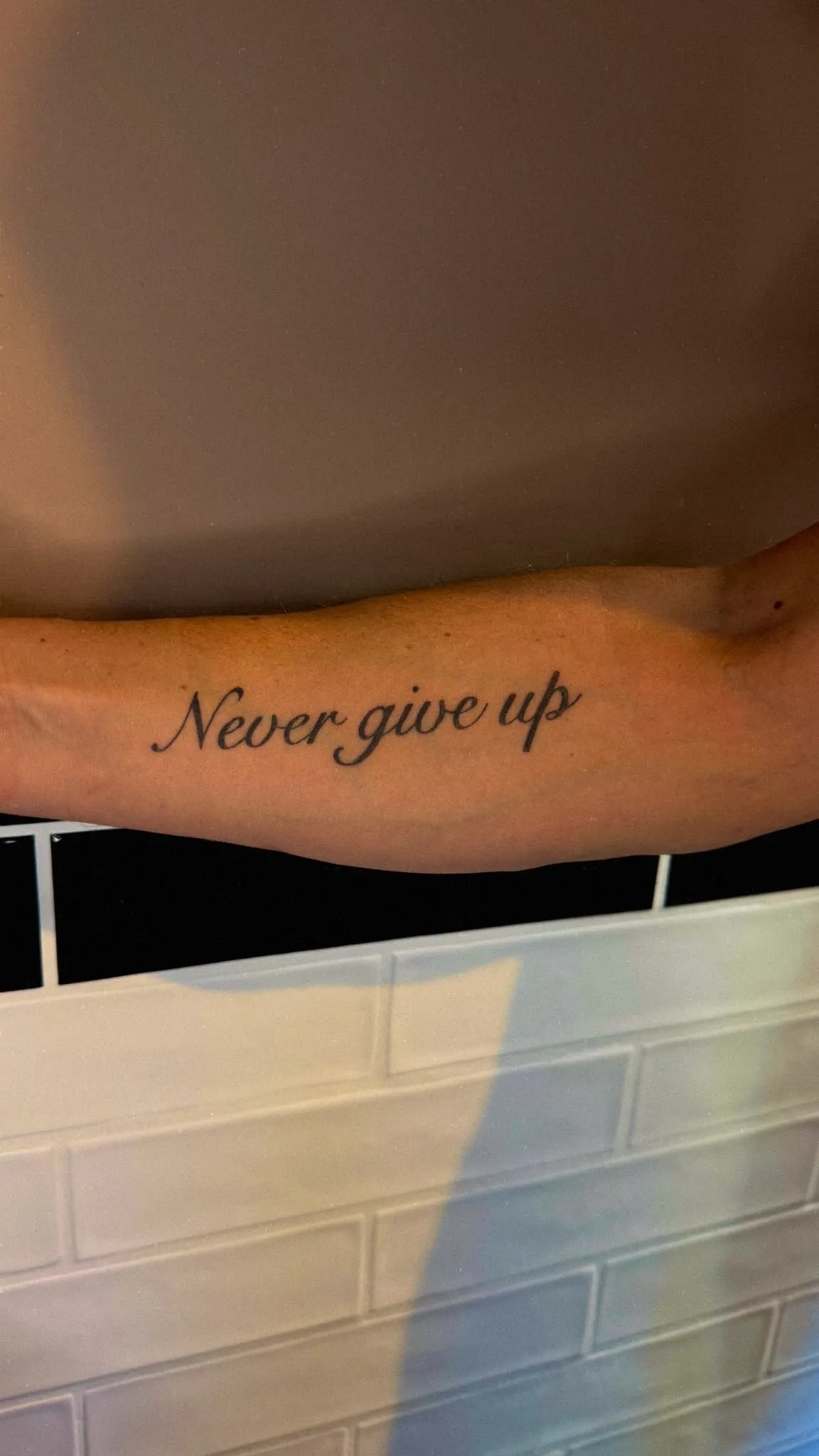 Tekst tattoo "Never give up" in sierlijk script op de onderarm