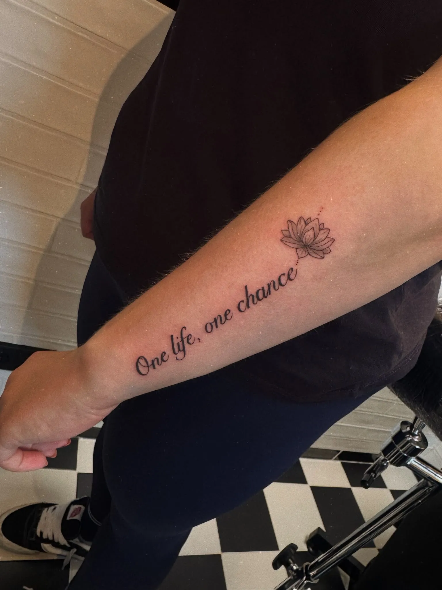 Tekst tattoo "One life, one chance" met een fineline lotus op de onderarm